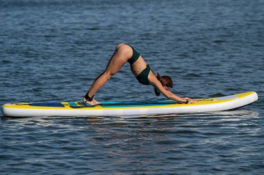 Beyaz kadın SUP panosunda yoga yapıyor.