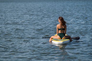 SUP panosunda poz veren beyaz bir kadın. Yaz sporu