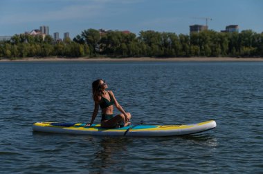 Beyaz kadın SUP panosunda yoga yapıyor.