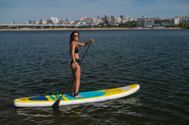 Gölde SUP sörf tahtası süren beyaz bir kadın. Yaz sporu