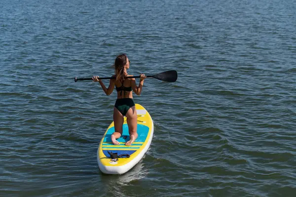 Gölde SUP sörf tahtası süren beyaz bir kadın. Yaz sporu