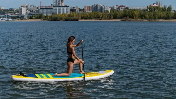 Gölde SUP sörf tahtası süren beyaz bir kadın. Yaz sporu