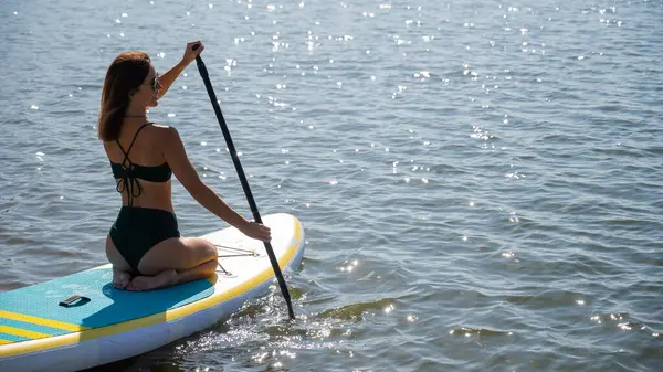 Güzel beyaz kadın SUP tahtasının üzerinde yüzüyor.