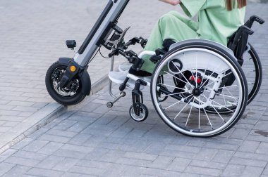 Tekerlekli sandalyedeki yüzü olmayan ve manuel kontrol için yardımcı bir aleti olan bir kadın. Elektrikli bisiklet.