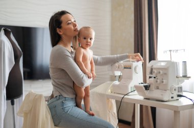 Genç bir kadın evde dikiş dikiyor ve kucağında küçük bir çocuk tutuyor. Annesi küçük oğluna dikiş makinesi dikmeyi öğretiyor..