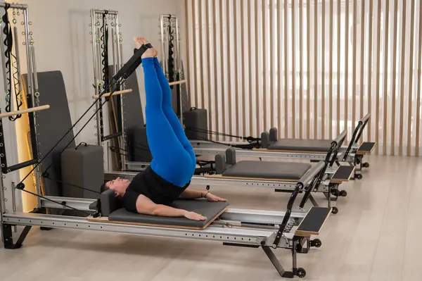 Aşırı kilolu beyaz kadın bir reformcu üzerinde pilates egzersizi yapıyor.