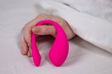Yatakta uzanırken kavisli pembe vibratör tutan kadın.