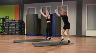 İki beyaz kadın spor salonunda burpee yapıyor.