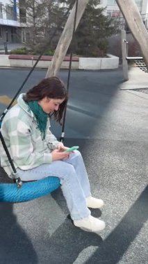 Beyaz kadın salıncakta sallanıyor ve akıllı telefon kullanıyor.