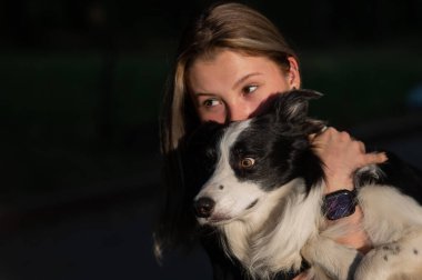 Beyaz bir kadın parkta yürürken köpeğine sarılıyor.