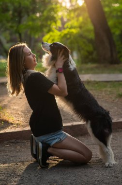 Beyaz bir kadın parkta yürürken köpeğine sarılıyor.