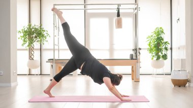 Tombul bir kadın stüdyoda pilates yapıyor.