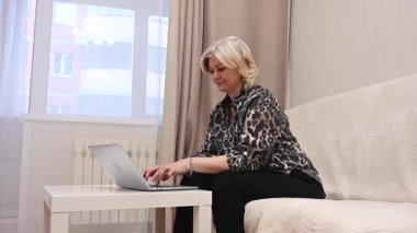 Kanepede otururken laptop kullanan olgun bir kadın.