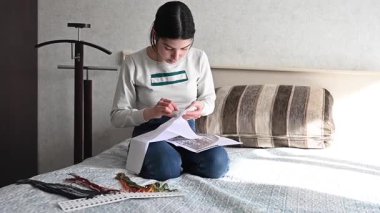 Genç beyaz kadın yatakta otururken çapraz dikiş atıyor.