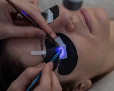 Kirpik uzatma prosedüründen geçen bir kadın ultraviyole lamba kullanıyor.