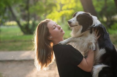 Beyaz bir kadın parkta yürürken köpeğine sarılıyor.