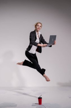 Beyaz arka planda dizüstü bilgisayarla atlayan takım elbiseli çıplak ayaklı balerin.