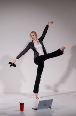 Beyaz arka planda iş elbisesiyle dans eden çıplak ayaklı balerin.