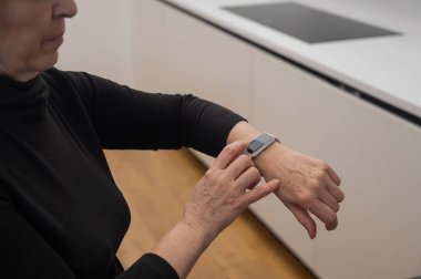 Kafkasyalı yaşlı bir kadın akıllı saate bakıyor. Ellerin yakın çekimi