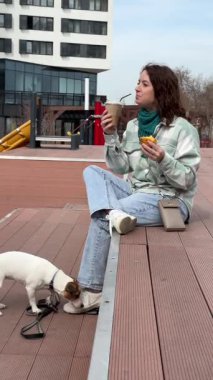Beyaz kadın kruvasan yiyip kahve içerken Jack Russell terrier köpeğini gezdiriyordu.