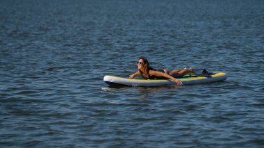 SUP panosunda poz veren beyaz bir kadın. Yaz sporu