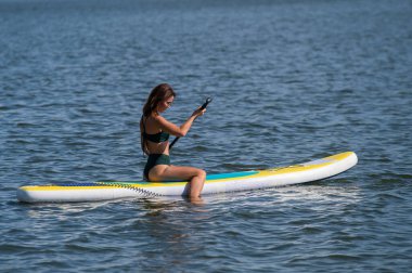Gölde SUP sörf tahtası süren beyaz bir kadın. Yaz sporu