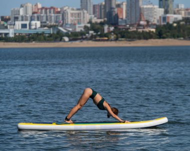 Beyaz kadın SUP panosunda yoga yapıyor.