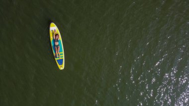 Gölde SUP sörf tahtası süren beyaz bir kadın. Yukarıdan bak. Yaz sporu