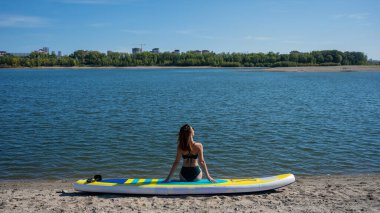 SUP panosunda poz veren beyaz bir kadın. Yaz sporu