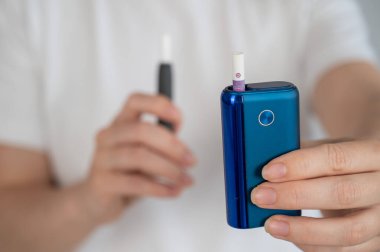 Bir kadın iki farklı tütün ısıtma sistemini karşılaştırır. Elektronik sigara.