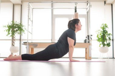 Tombul bir kadın stüdyoda pilates yapıyor.