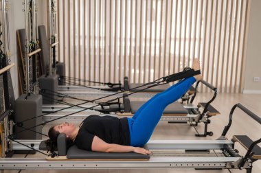 Aşırı kilolu beyaz kadın bir reformcu üzerinde pilates egzersizi yapıyor.