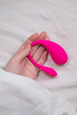 Yatakta uzanırken kavisli pembe vibratör tutan kadın.