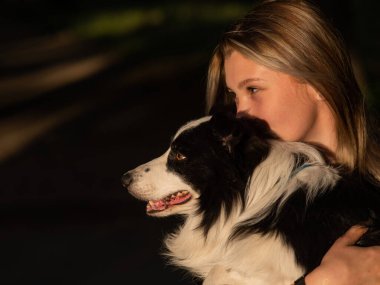 Beyaz bir kadın parkta yürürken köpeğine sarılıyor.