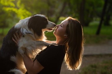Beyaz bir kadın parkta yürürken köpeğine sarılıyor.