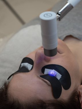 Kirpik uzatma prosedüründen geçen bir kadın ultraviyole lamba kullanıyor.