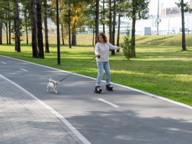 Beyaz kadın, Jack Russell Terrier köpeğiyle parkta paten kayıyor.