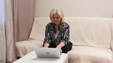 Kanepede otururken laptop kullanan olgun bir kadın.