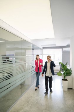 İki meslektaş ofiste yürüyor ve telefonda konuşuyorlar.