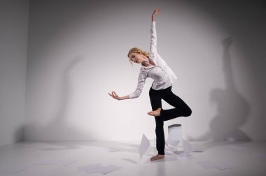 Takım elbiseli zarif bir balerin belgeleri fırlatır. İş kadını beyaz arka planda yalınayak dans ediyor..