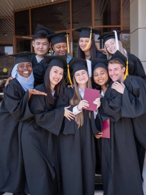 Farklı uluslardan mutlu öğrenciler mezuniyet elbiseleriyle diplomalarını tutuyorlar.