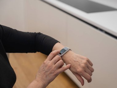 Kafkasyalı yaşlı bir kadın akıllı saate bakıyor. Ellerin yakın çekimi