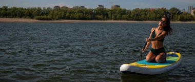 Gölde SUP sörf tahtası süren beyaz bir kadın. Yaz sporu