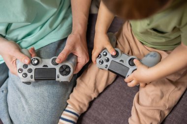 Beyaz kadın küçük oğluna konsol oynamayı öğretiyor. Oyun kolu ellerinde.