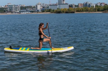 Gölde SUP sörf tahtası süren beyaz bir kadın. Yaz sporu