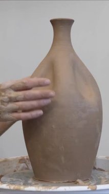 Çömlekçi ellerinin çömlekçi çarkında seramik sürahi yapmasının yakın çekimi. Dikey video