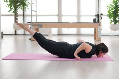 Tombul bir kadın stüdyoda pilates yapıyor.