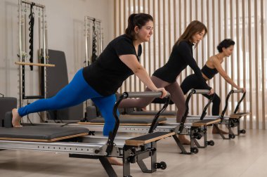 Üç Asyalı kadın bir reformcu üzerinde pilates yapıyor.