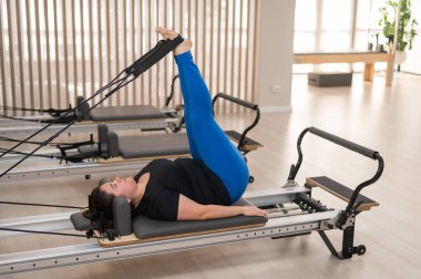 Aşırı kilolu beyaz kadın bir reformcu üzerinde pilates egzersizi yapıyor.