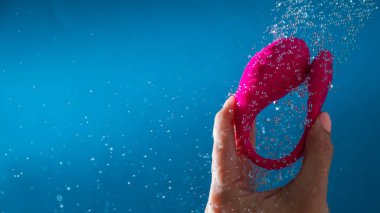 Duşta pembe vibratörü yıkayan kadın. Mavi arka planda su geçirmez seks oyuncağı